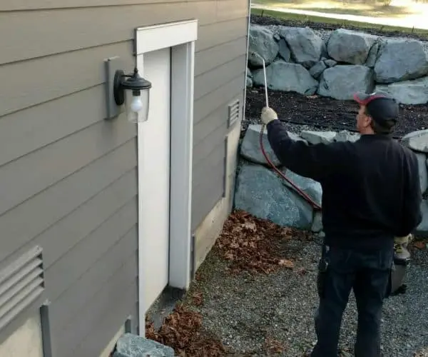 Pest control technician applying exterior pest treatment around a home